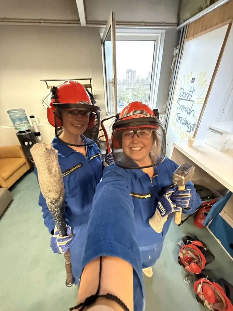 Two people smiling in rage room gear ready to smash