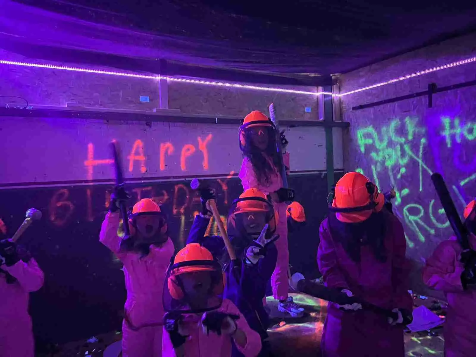 Large group enjoying the ultimate glow in the dark rage room experience in Amsterdam while smashing electronics, furniture, and breakables under neon lighting and immersive UV effects.